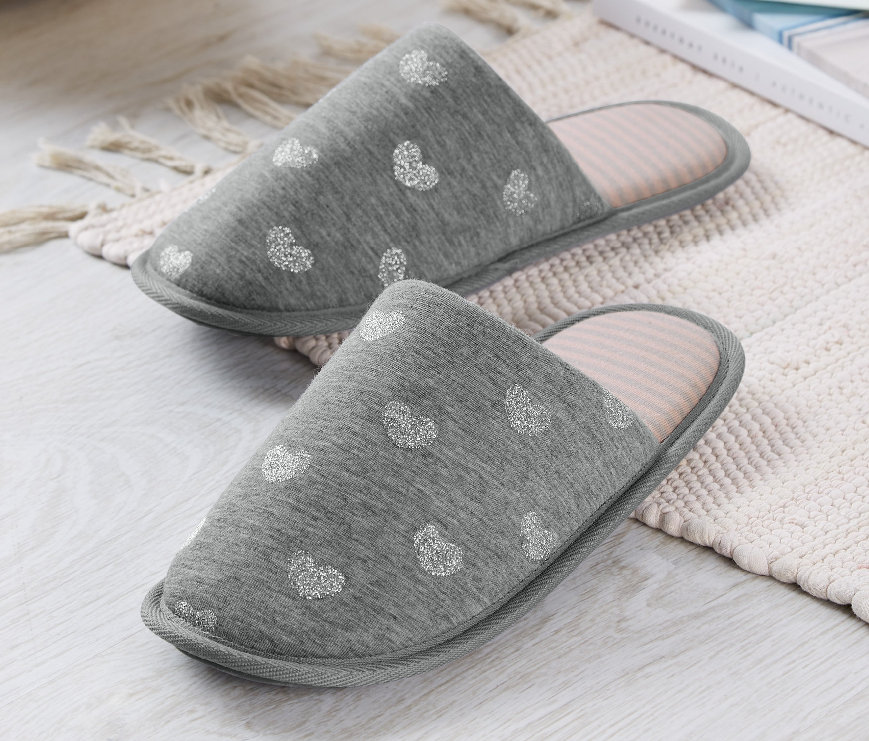 Dva šedé pantofle s bílým vzorem srdce na krémovém koberci.