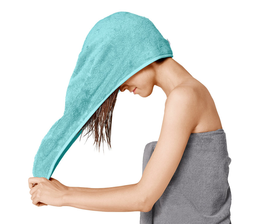Žena si dává na mokré vlasy ručníkový turban.