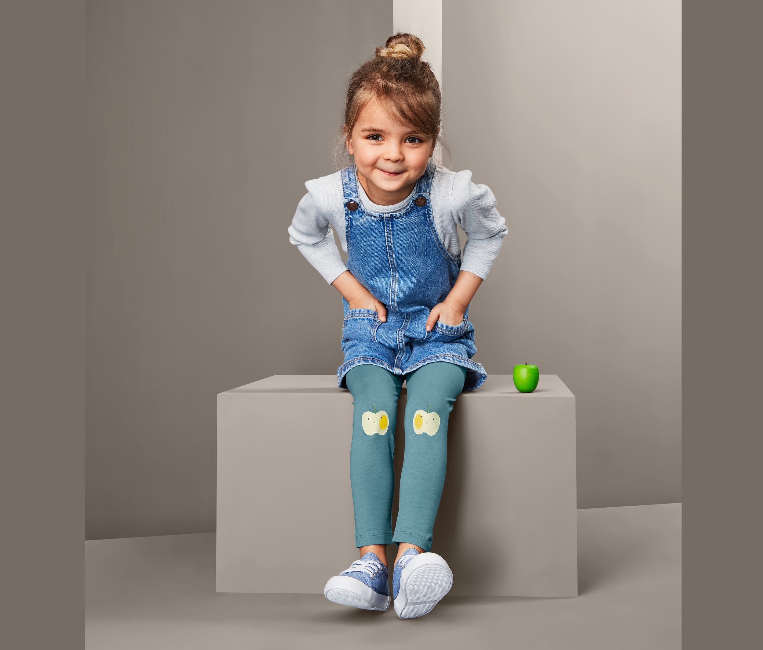 Dívka sedí a má na sobě džínové šaty a 2 ks legín s nášivkami kuřátek.
