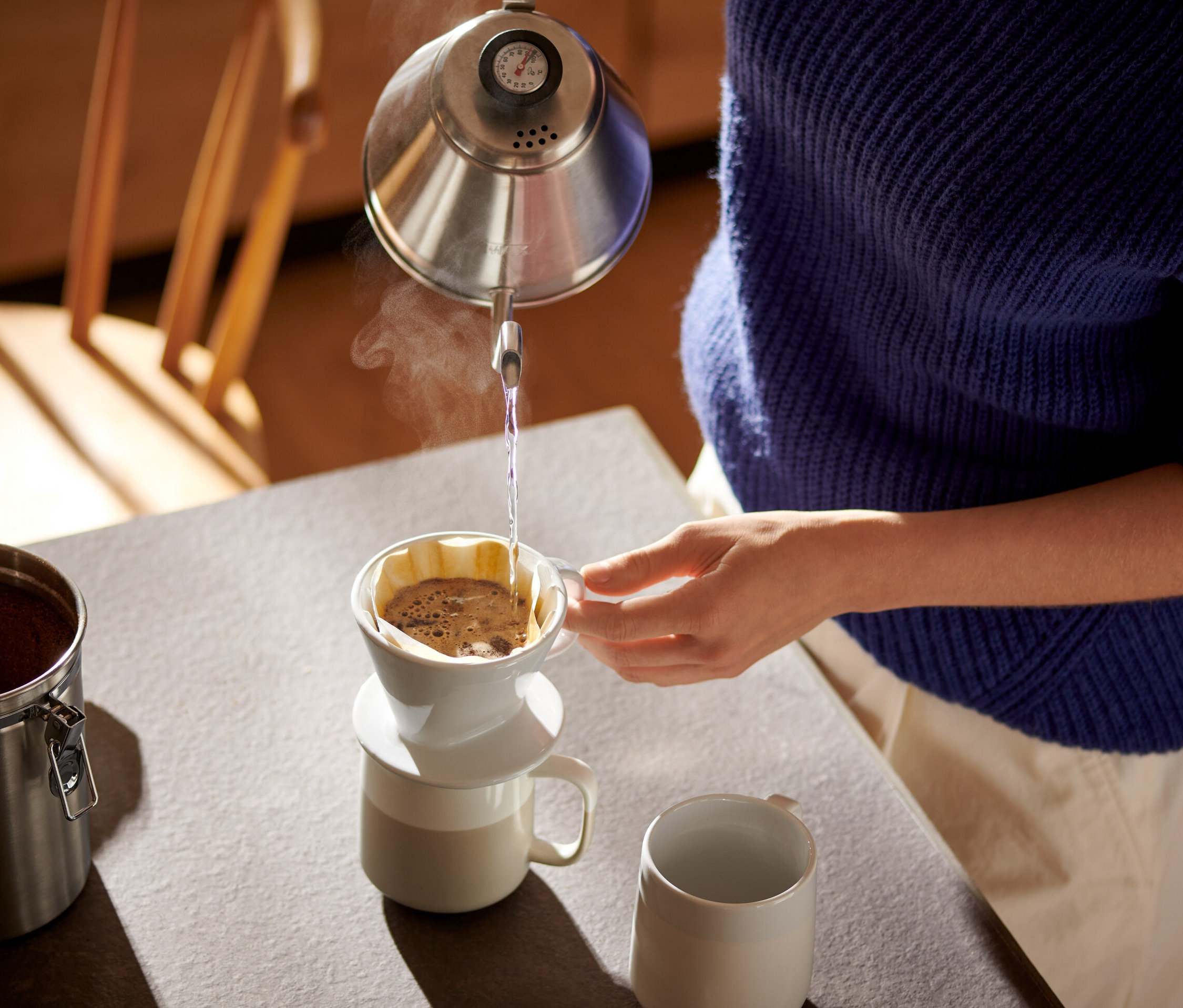 Žena nalévá vodu z konvice do bílého ručního kávového filtru vel. 101 s papírovým filtrem na kávu vel. 101.