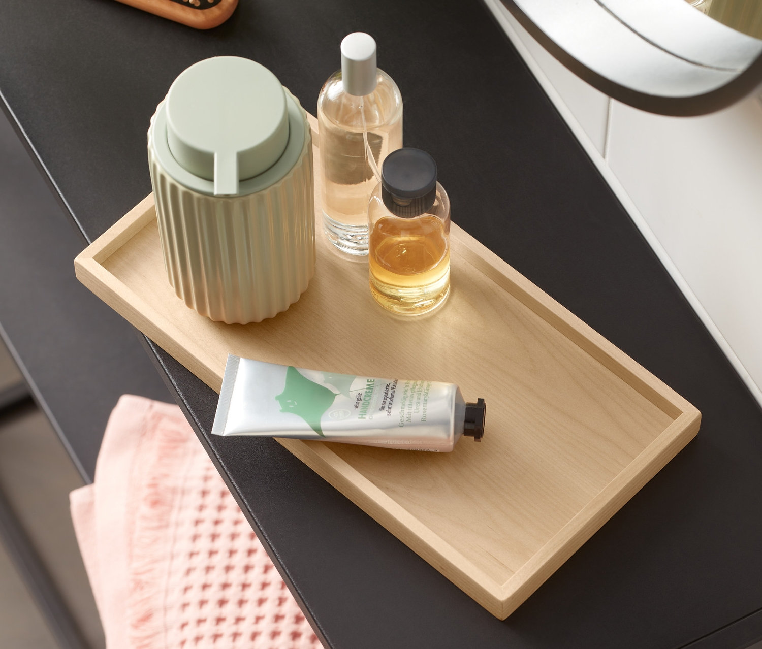 Toaletní stolek s dřevěným podnosem, dávkovačem mýdla, lahvičkami a ručníkem.