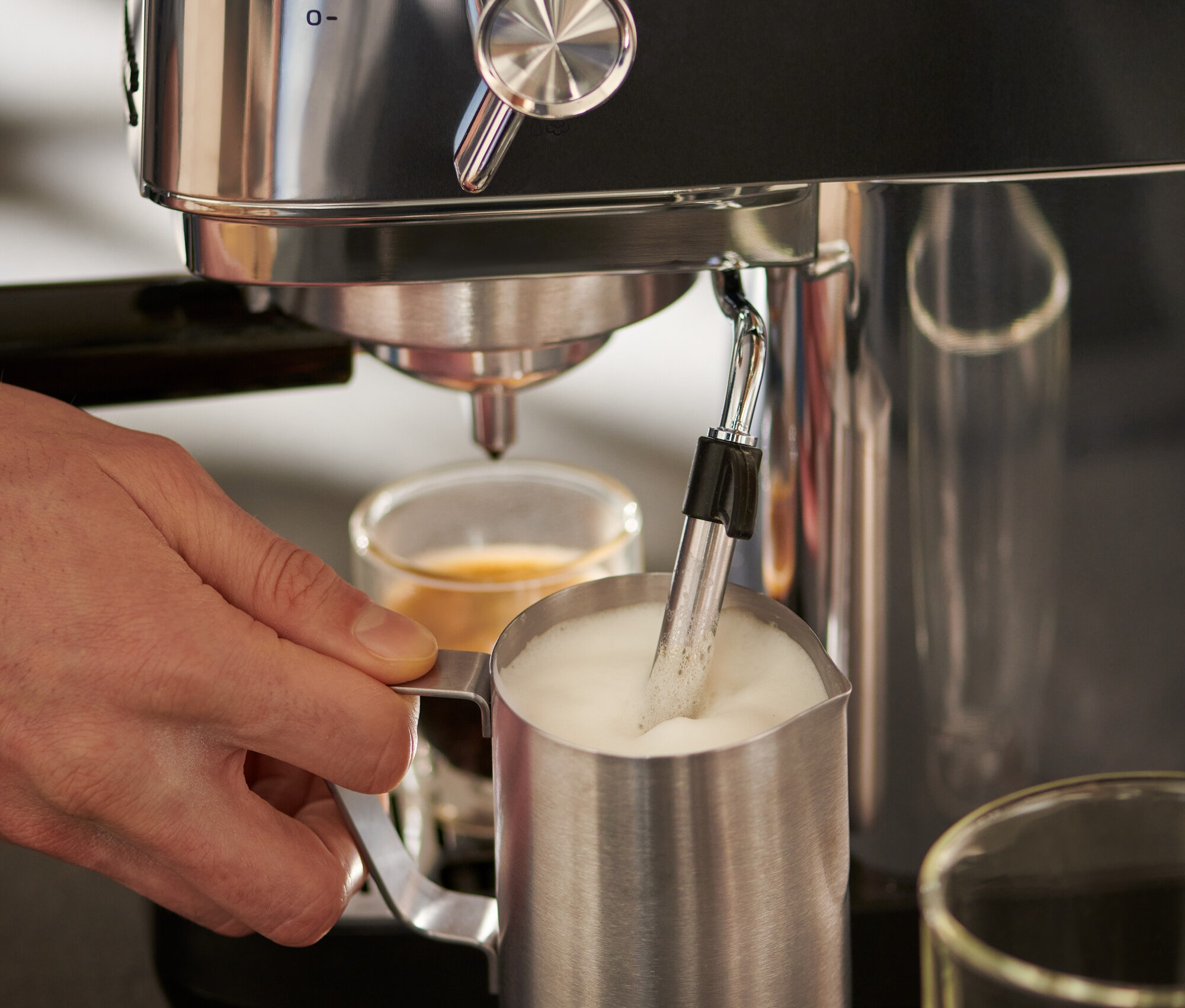 Muž používá stříbrný pákový kávovar »Lapressa« a nerezovou konvičku na mléko (300 ml).