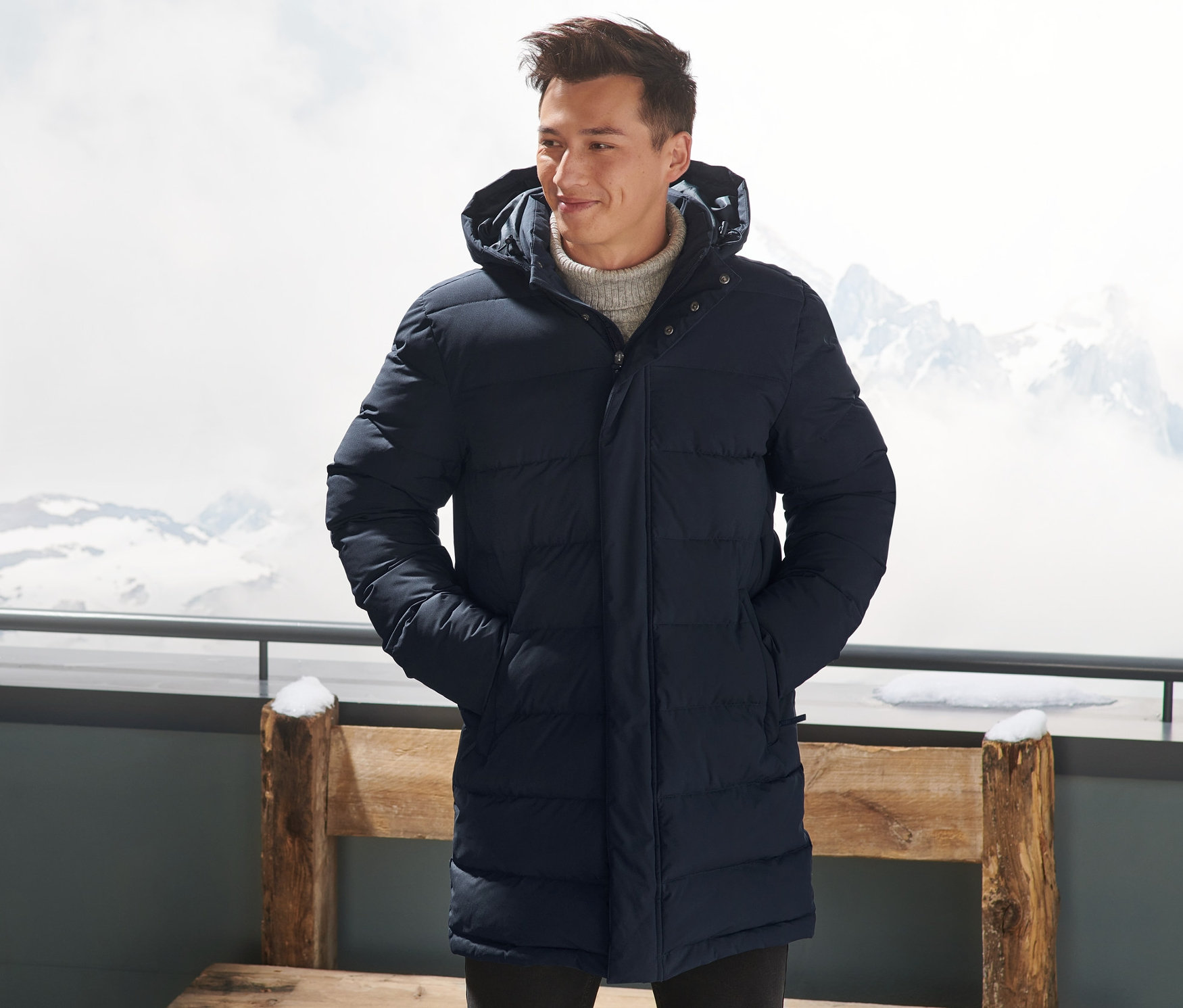 Muž v tmavě modré péřové prošívané parke stojí venku s rukama v kapsách.