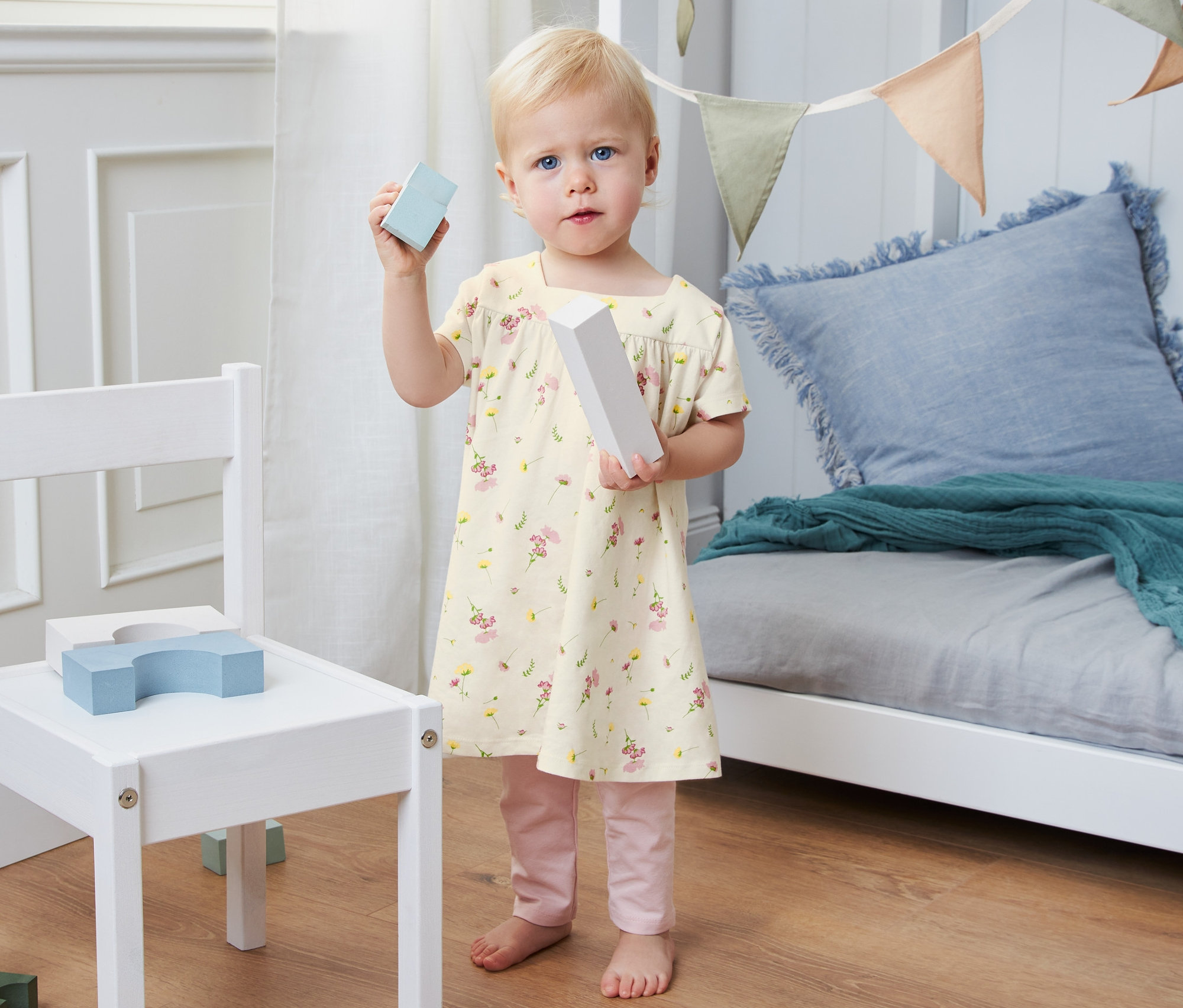 Batole drží kostky v ruce a má na sobě žerzejové šaty z biobavlny.