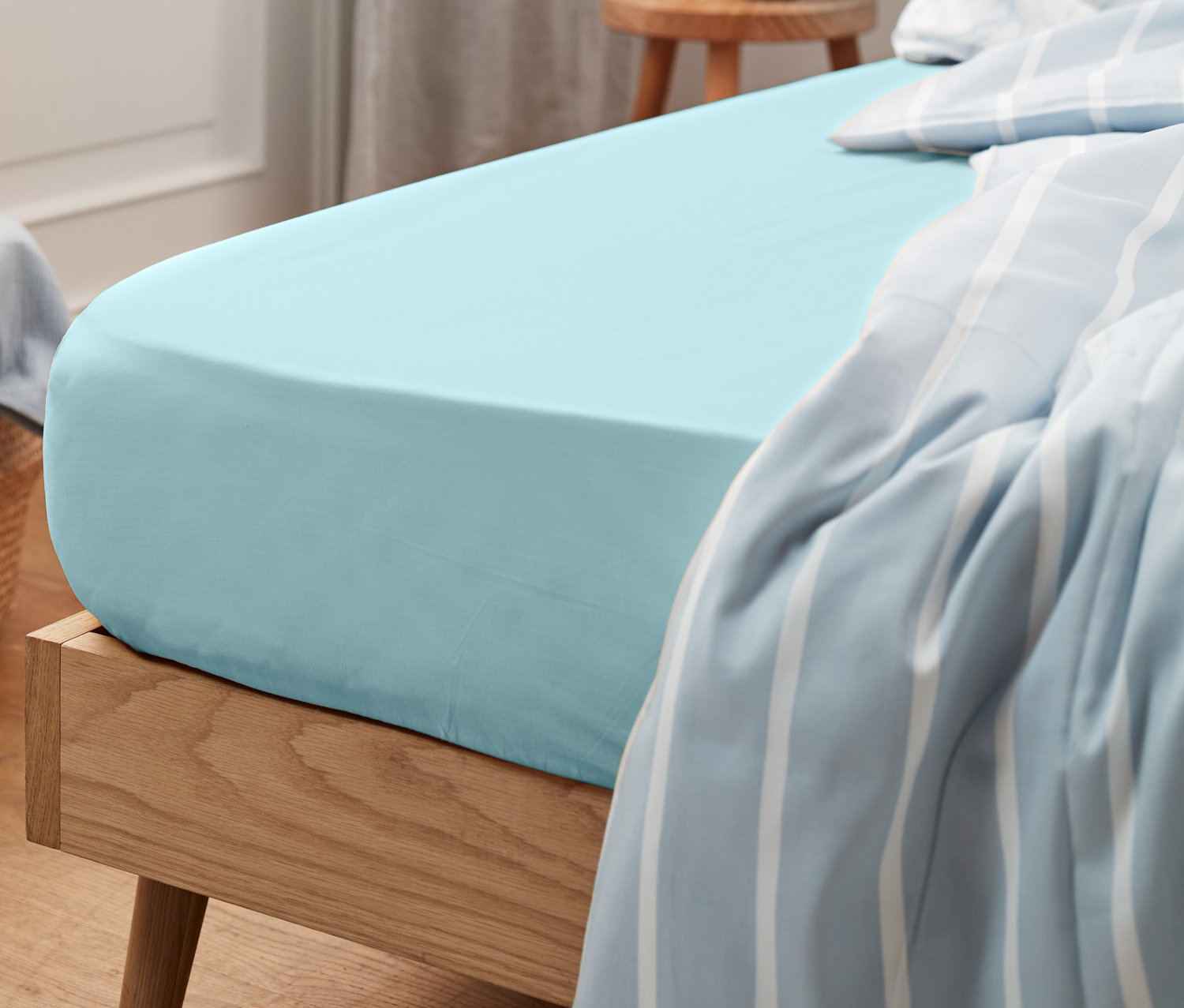 Detail modrého žerzejového prostěradla na posteli s dřevěným rámem.