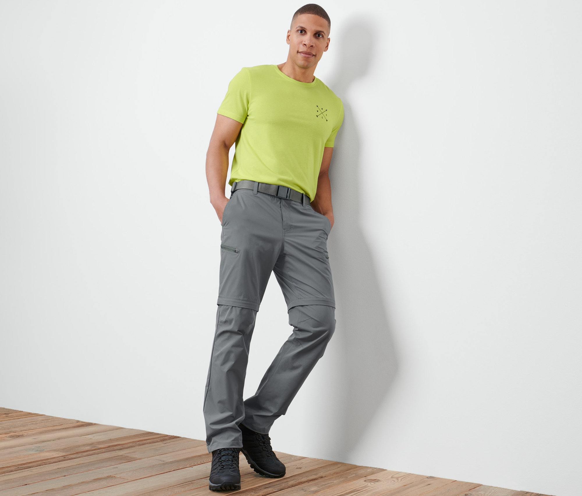 Muž opřený o zeď má na sobě šedé funkční kalhoty 2 v 1.