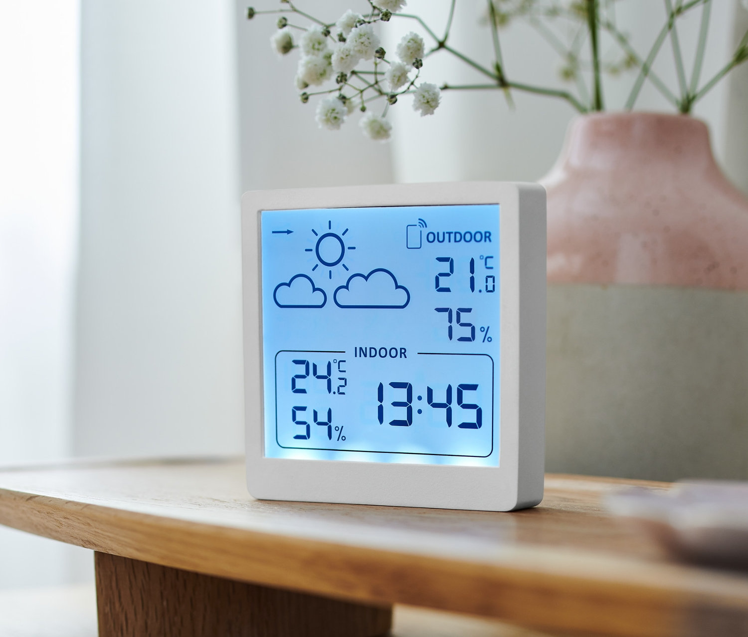 Bílá meteostanice zobrazuje vnitřní a venkovní teplotu a vlhkost vzduchu.