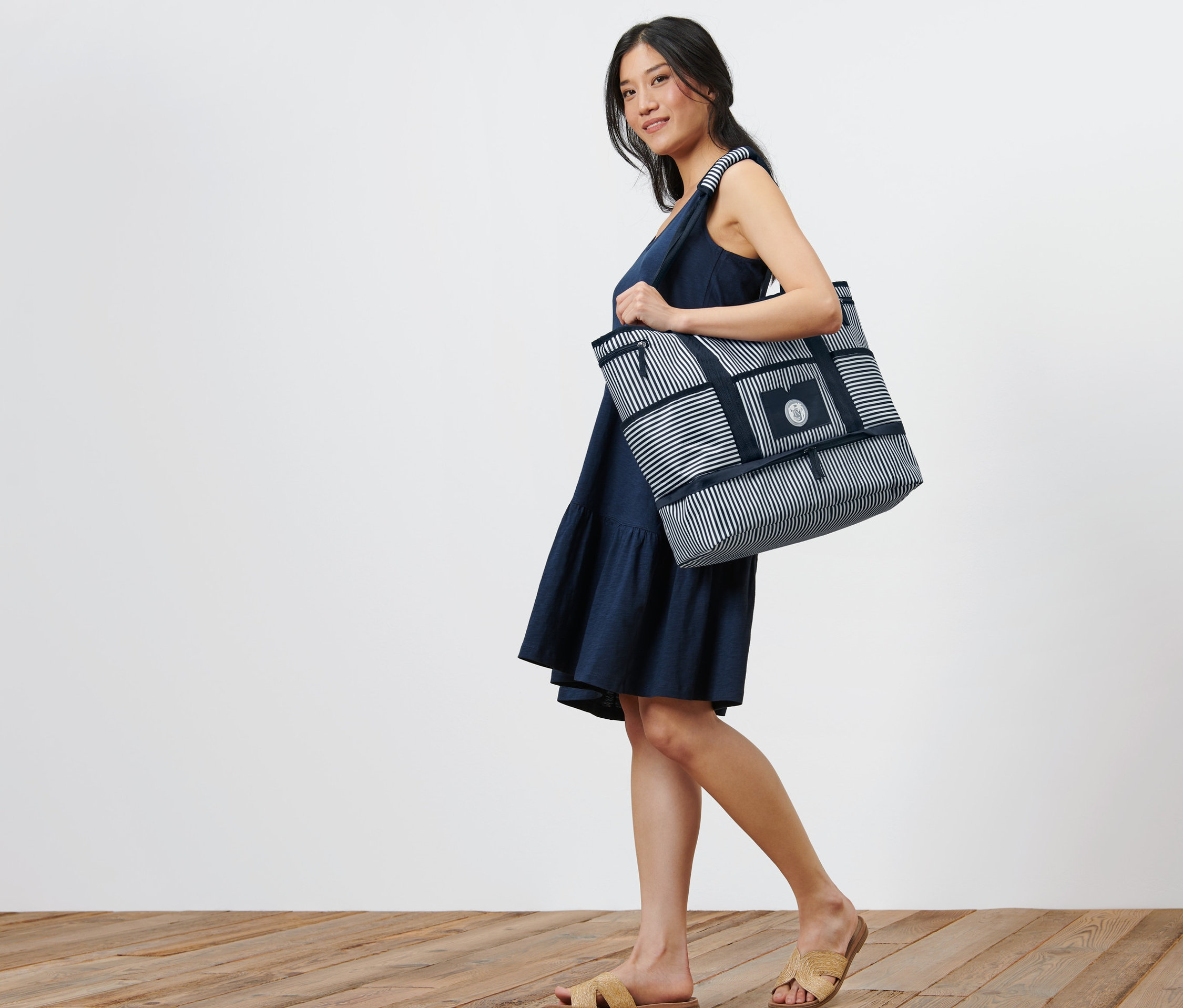 Žena nese plážovou tašku s modrými a bílými pruhy.