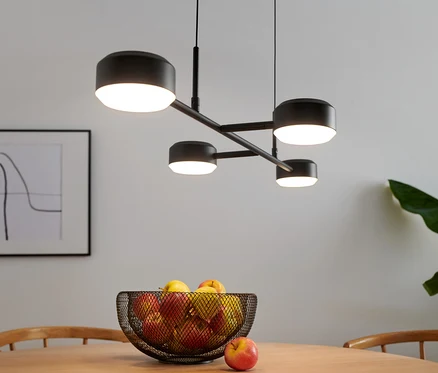 Čtyřramenná LED lampa visí nad stolem s ovocem.