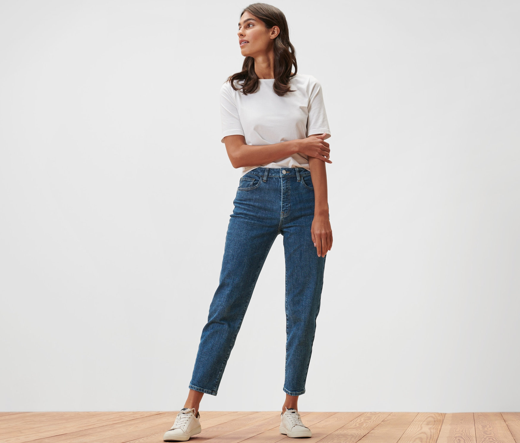 Žena stojící na dřevěné podlaze v džínách Mom Fit »Nyla« a bílém tričku.