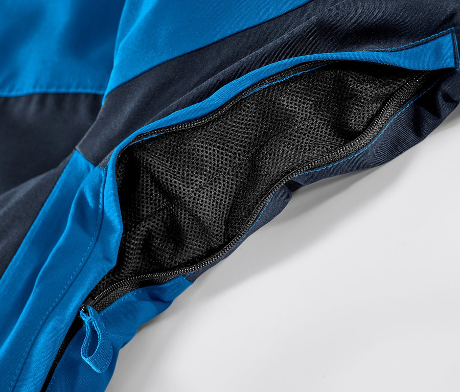 Detail modré lyžařské bundy s otevřenou kapsou na zip.