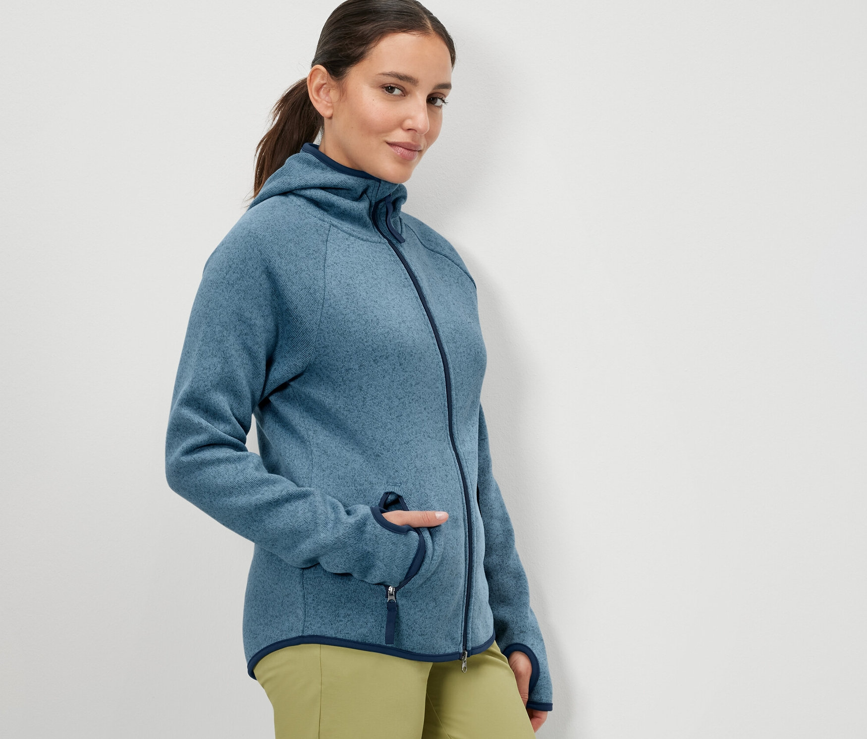 Žena pózuje v tmavě modré bundě z pleteného fleecu.