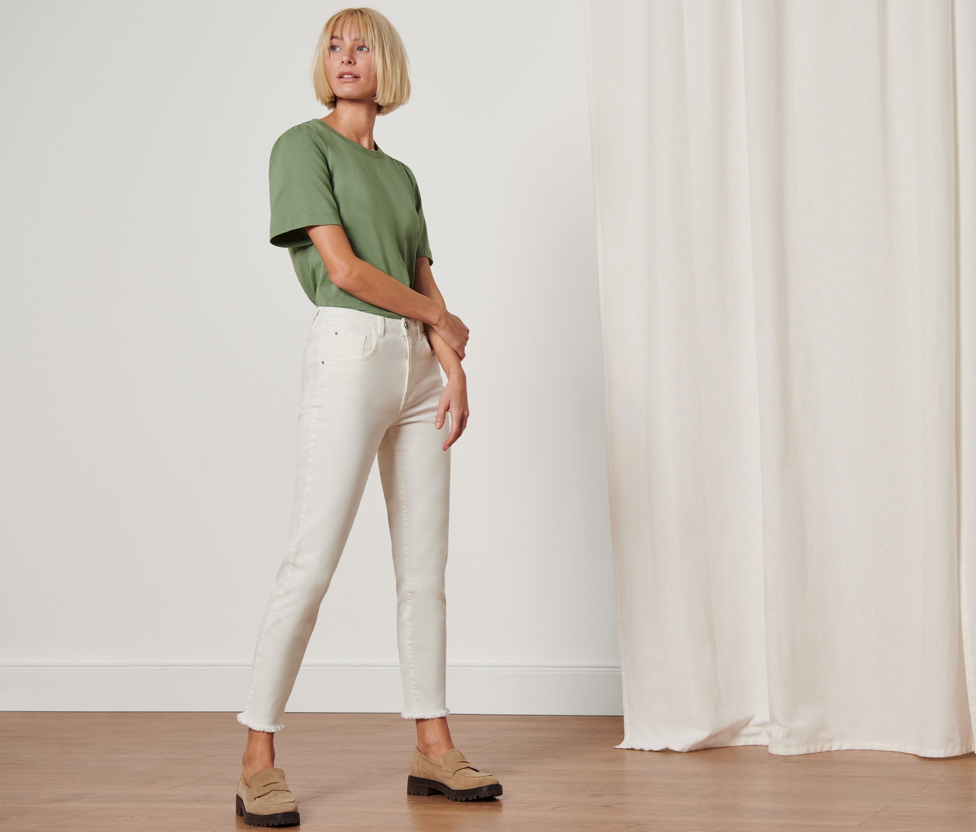 Žena pózuje v moderních džínách »Fit Lilly« a zeleném tričku.