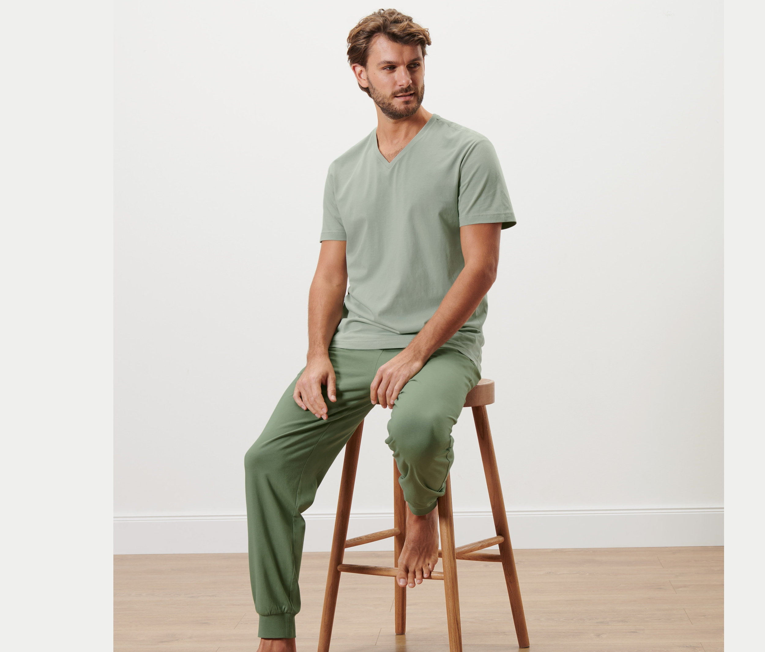 Muž sedí na dřevěné stoličce a má na sobě pyžamo.
