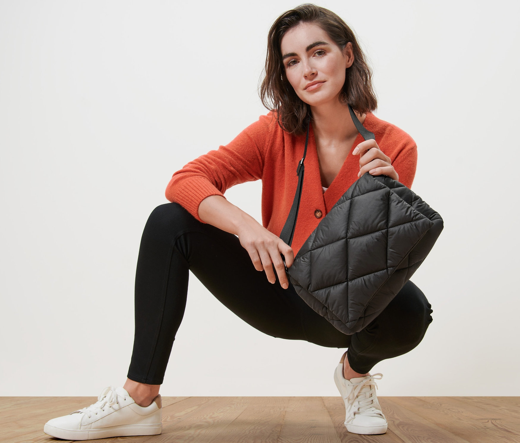 Žena v oranžovém svetru drží prošívanou tašku přes rameno.