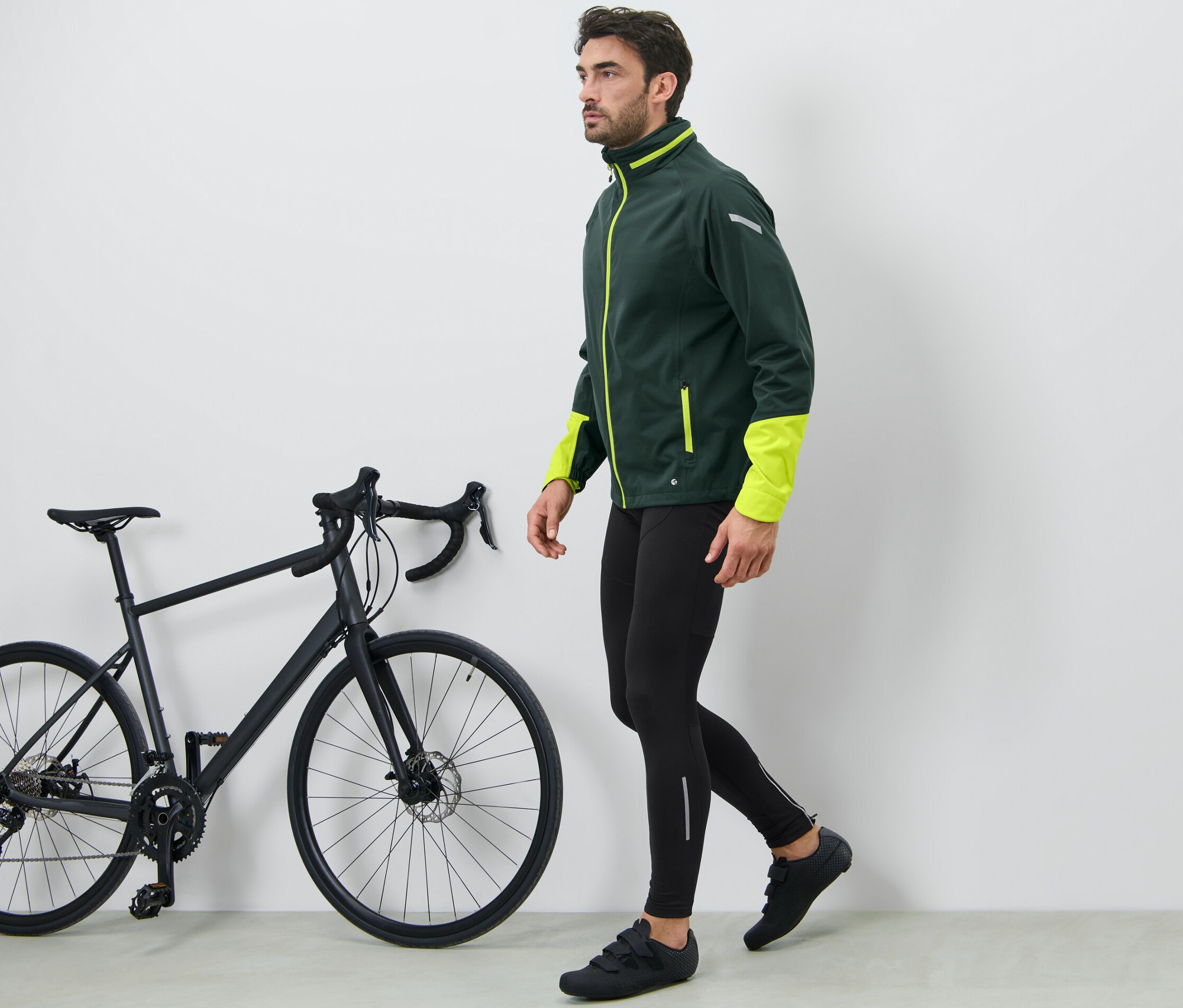 Muž kráčí vedle černého kola a má na sobě cyklistické kalhoty.