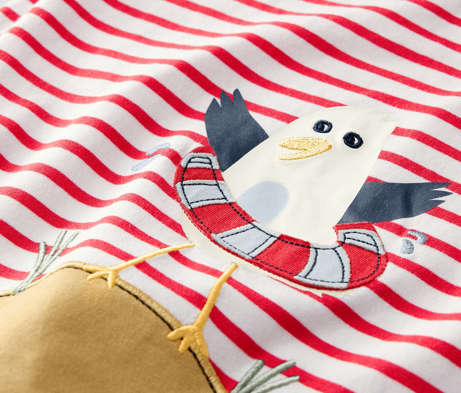 Detail dětského trička s červenými pruhy a aplikací racka s plavacím kruhem.