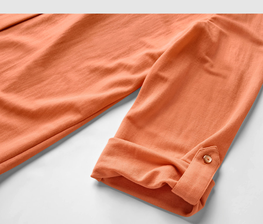 Detail broskvové halenky z žerzejového piké s ohrnutými rukávy.