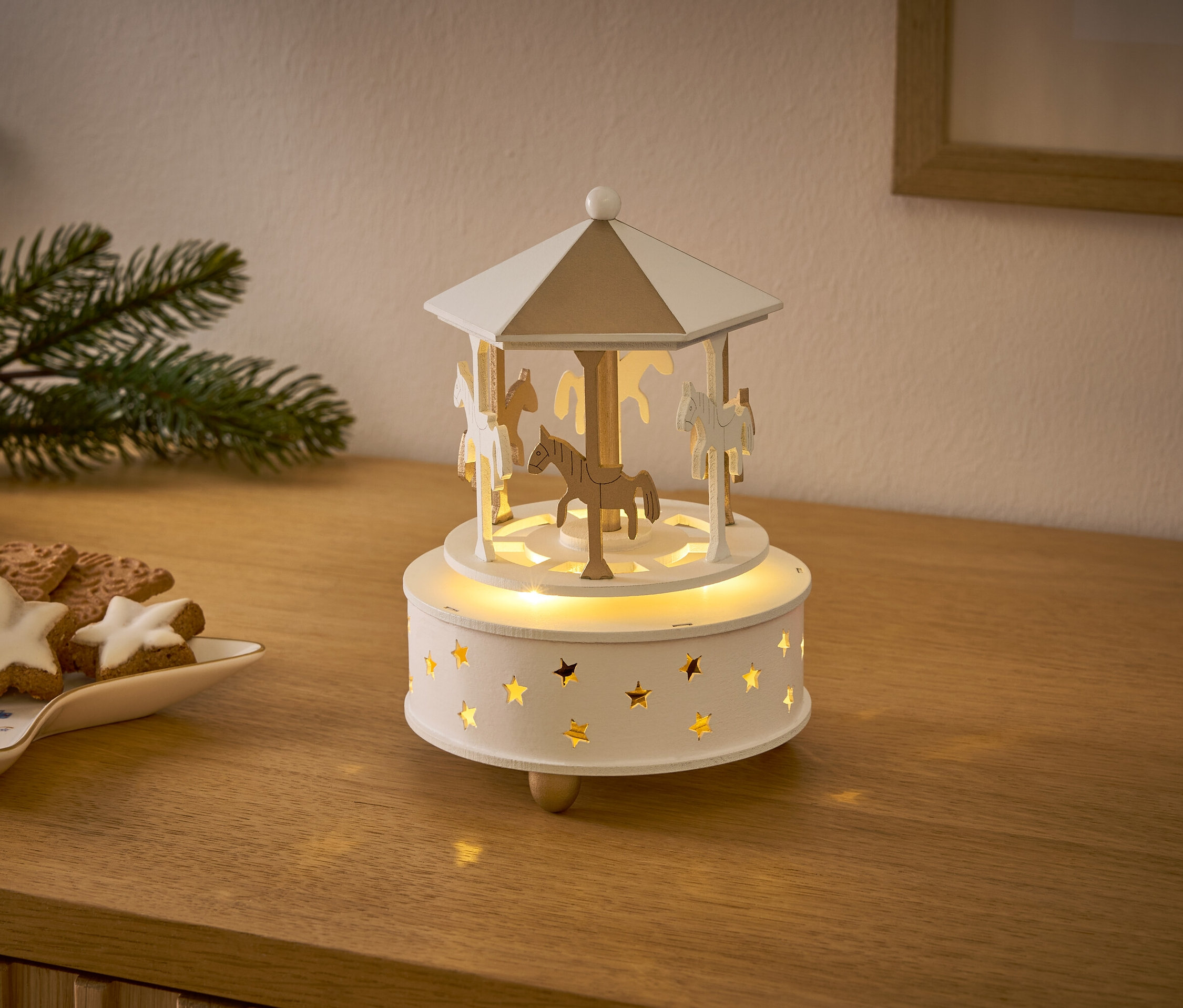 Dřevěný kolotoč s koni a hvězdami svítí na dřevěném stole vedle vánočních sušenek.