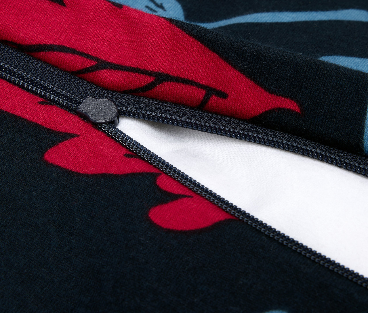 Detailní záběr na zip na tmavě modrém povlečení s červenými a modrými květy.