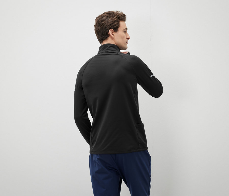 Muž v černém svetru se zipem a modrých kalhotách se dívá doleva.