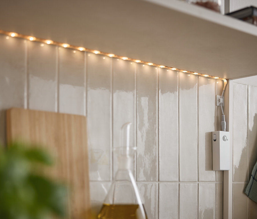 LED pásek svítí pod skříňkou na bílých dlaždicích.