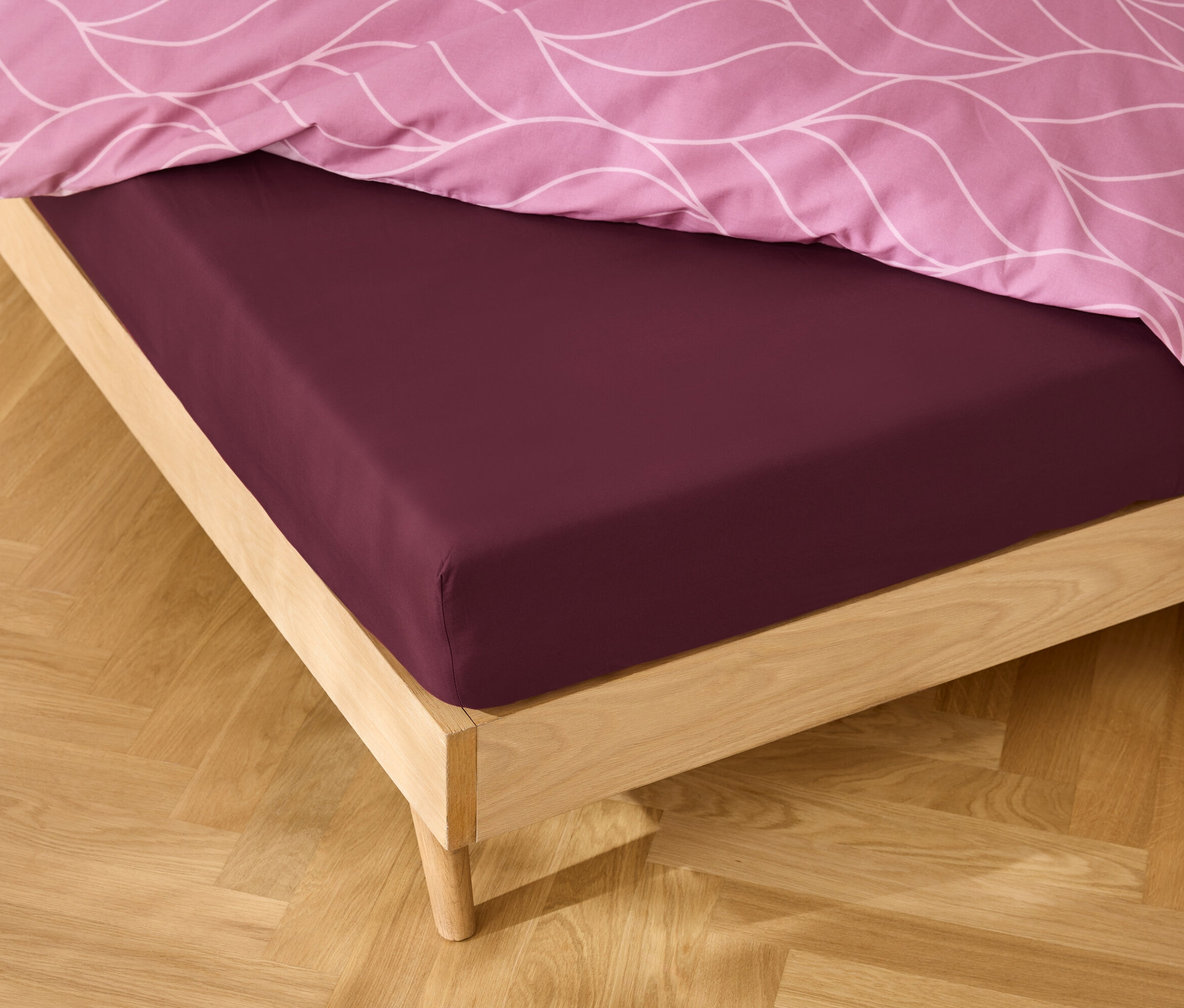 Čelo postele s bordó prostěradlem a růžovým vzorovaným povlečením.