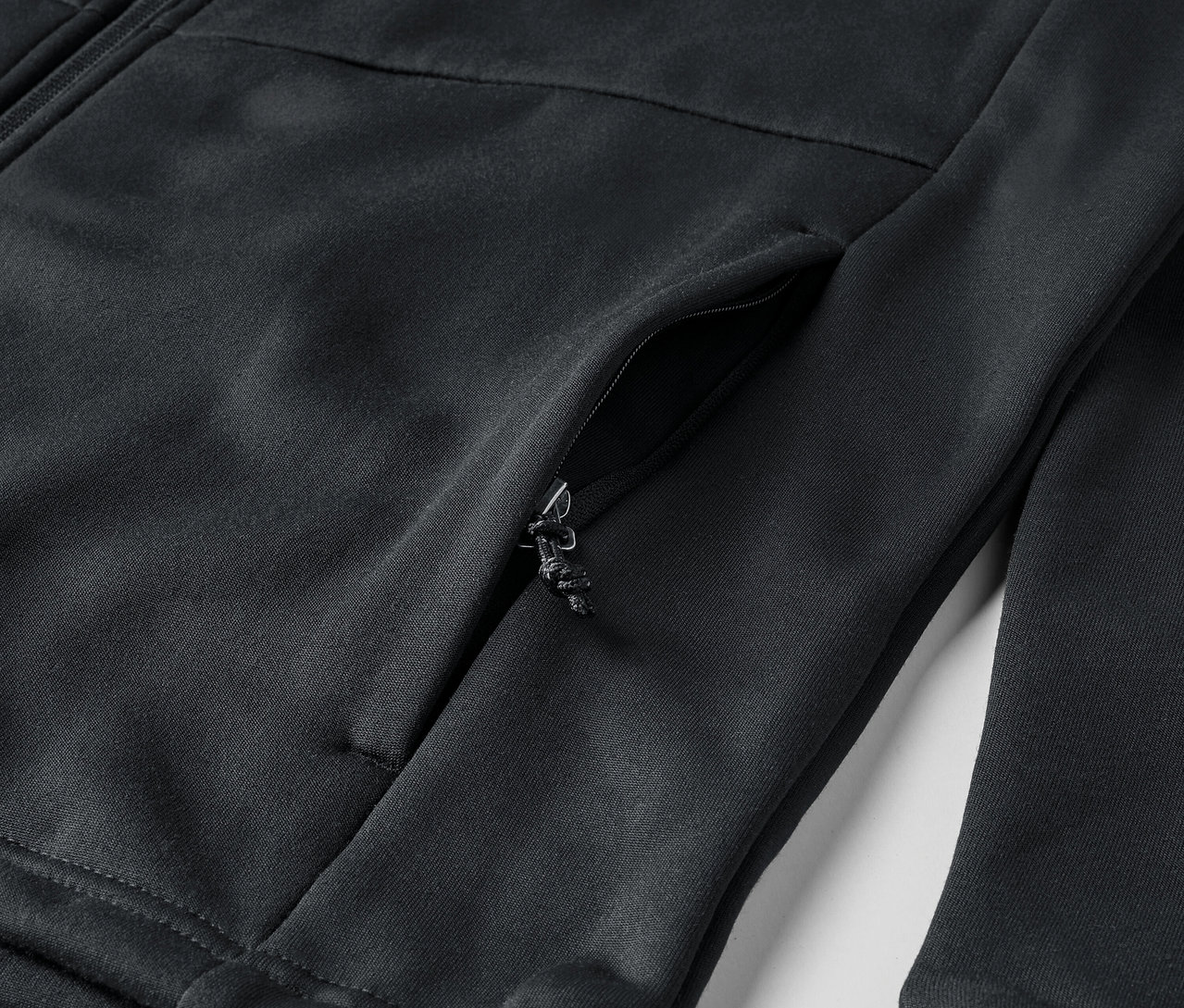Detail černé mikiny se zipem a kapsou.
