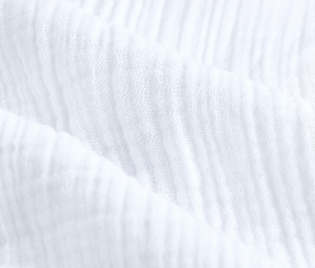 Detailní záběr bílého mušelínového povlečení standardní velikosti.