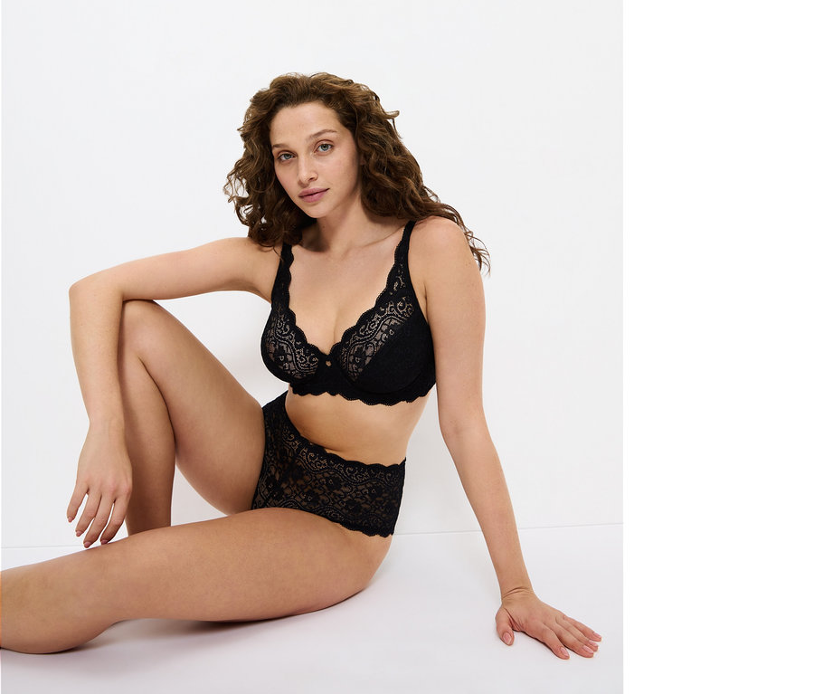 Žena sedí na zemi a má na sobě černou krajkovou podprsenku a kalhotky.