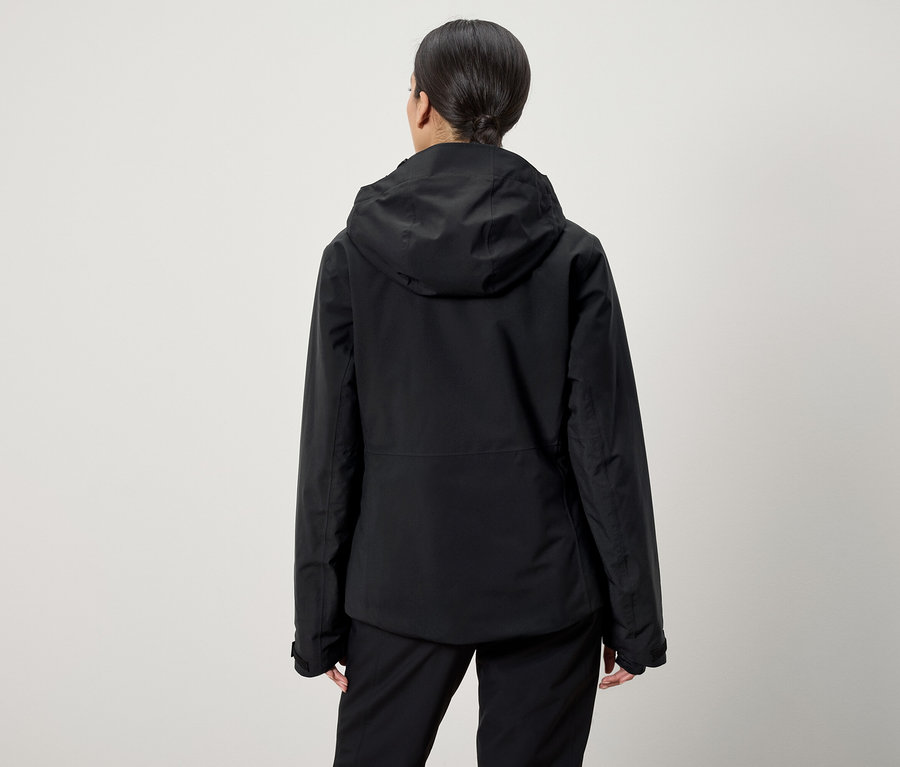 Zezadu je vidět žena s vlasy staženými do culíku, která má na sobě černou bundu s kapucí a černé kalhoty.