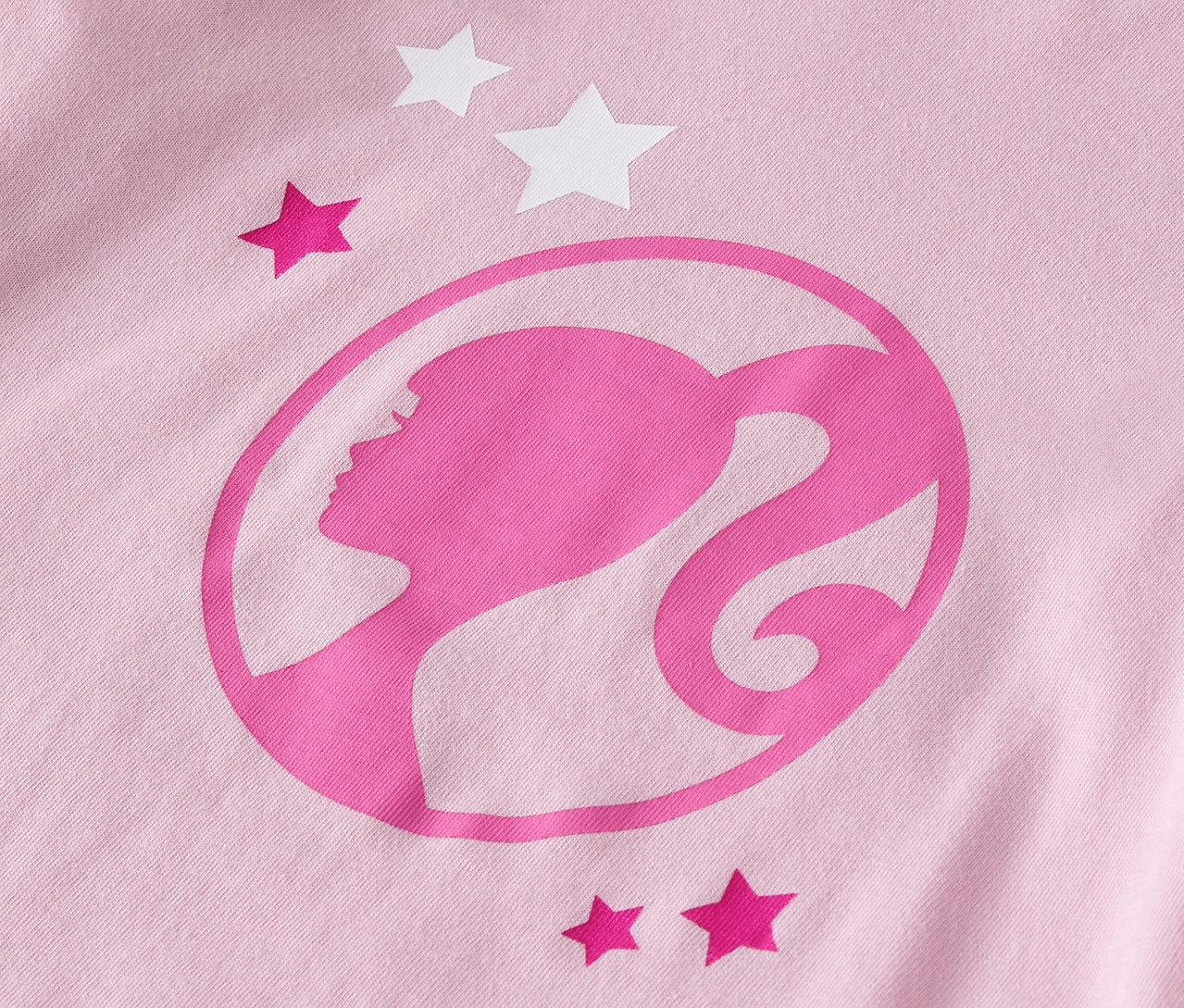 Detail růžového trička s logem Barbie a hvězdami.
