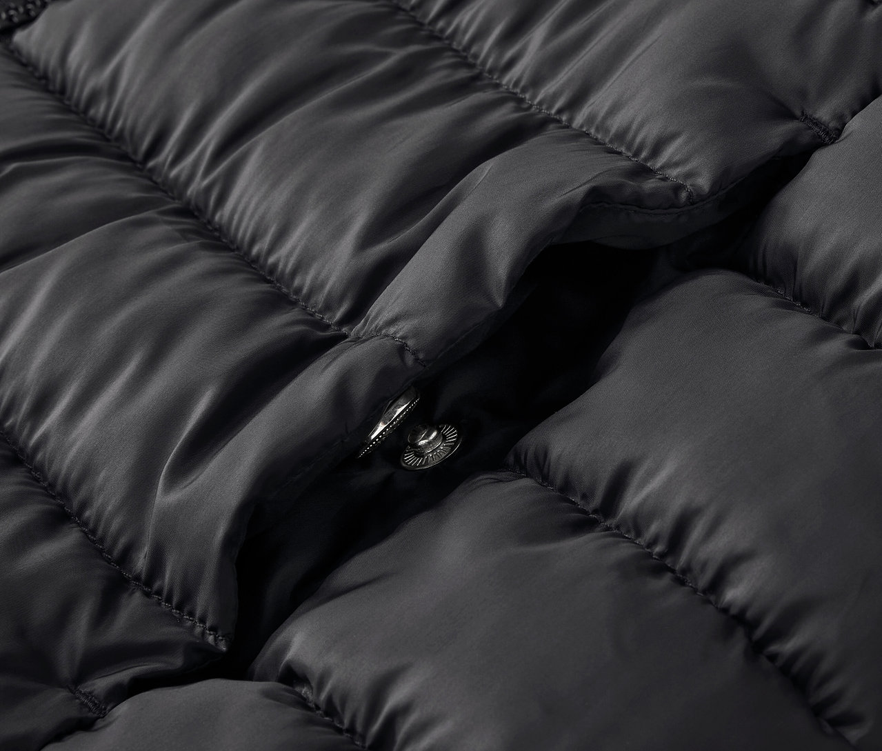 Detail černé prošívané bundy s patentkou.