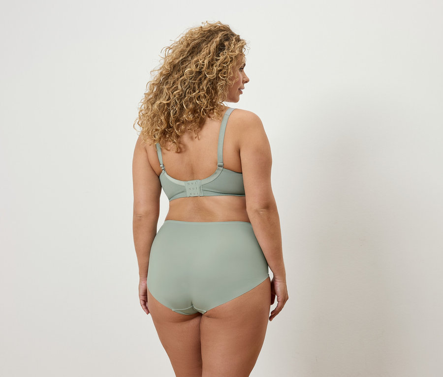 Žena s kudrnatými vlasy stojí zády a má na sobě světle zelenou podprsenku a kalhotky.