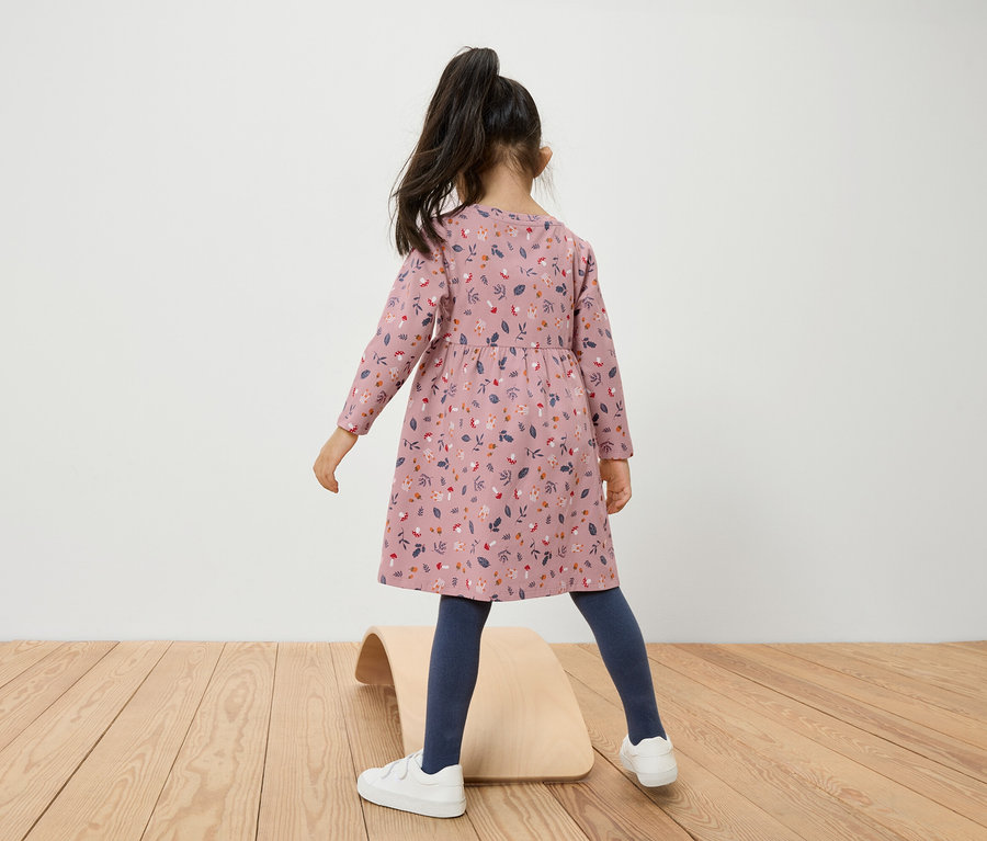 Dívka v květinových šatech stojí na dřevěné balanční desce.