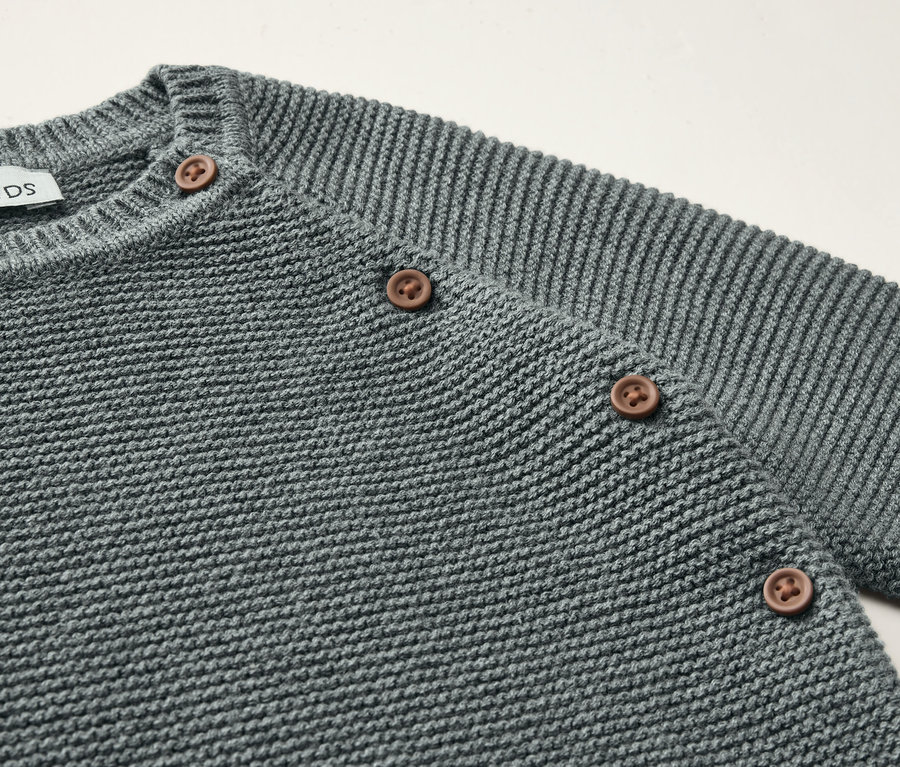 Detail šedé pletené soupravy pro miminka s hnědými knoflíky.