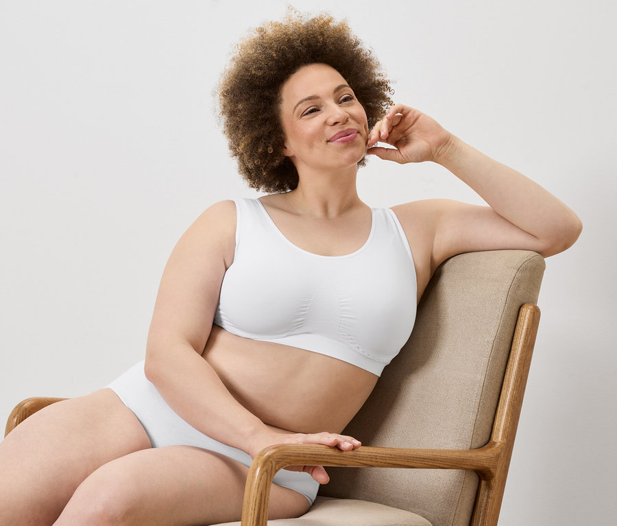 Žena s afro účesem sedí v křesle v bílé podprsence a kalhotkách.