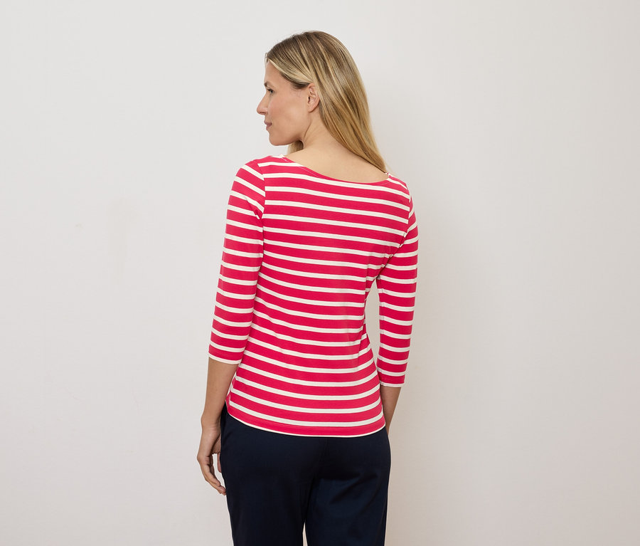 Blondýna se dívá doleva a má na sobě červenobílé pruhované tričko s tříčtvrtečním rukávem.
