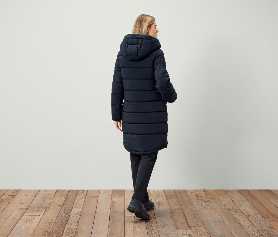 Žena v tmavě modré prošívané bundě s kapucí, záda k fotoaparátu.