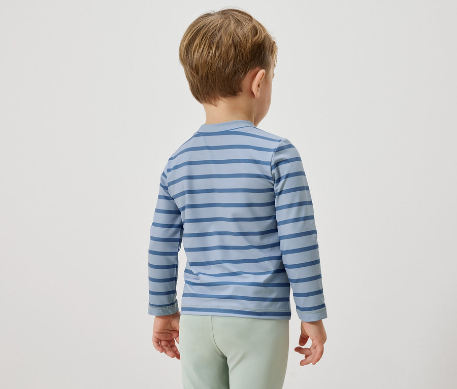 Dítě zezadu, má na sobě modré pruhované tričko s dlouhým rukávem a světle zelené kalhoty.