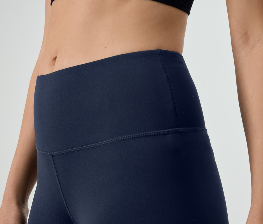 Detailní záběr na ženu v tmavě modrých legínách a černém sportovním topu.