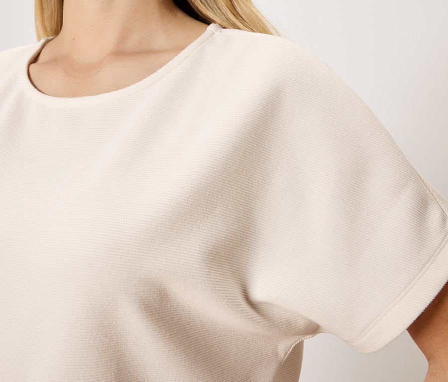 Detailní záběr ženy ve světle béžovém topu s krátkým rukávem a kulatým výstřihem.