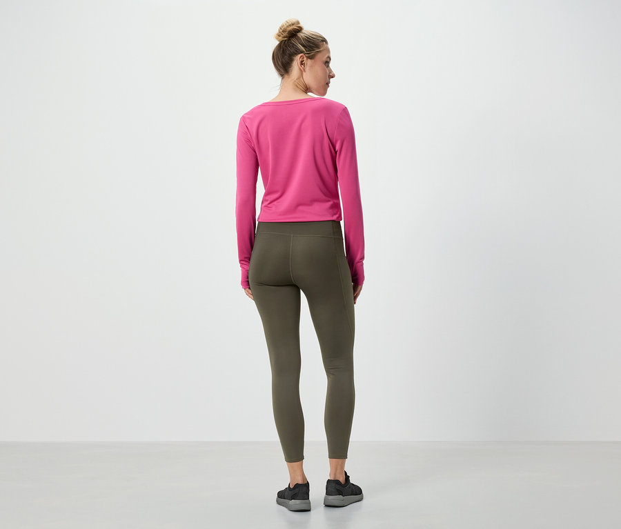 Žena stojí zády ke kameře a má na sobě růžové tričko s dlouhým rukávem a olivově zelené legíny.
