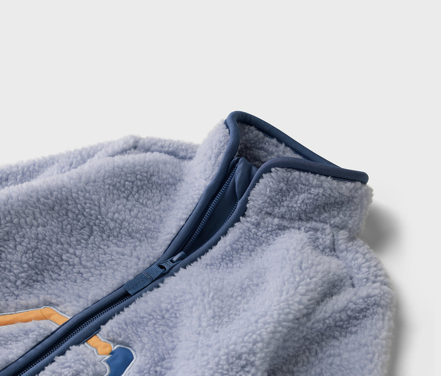 Detailní záběr na světle modrou fleecovou bundu s modrým zipem.