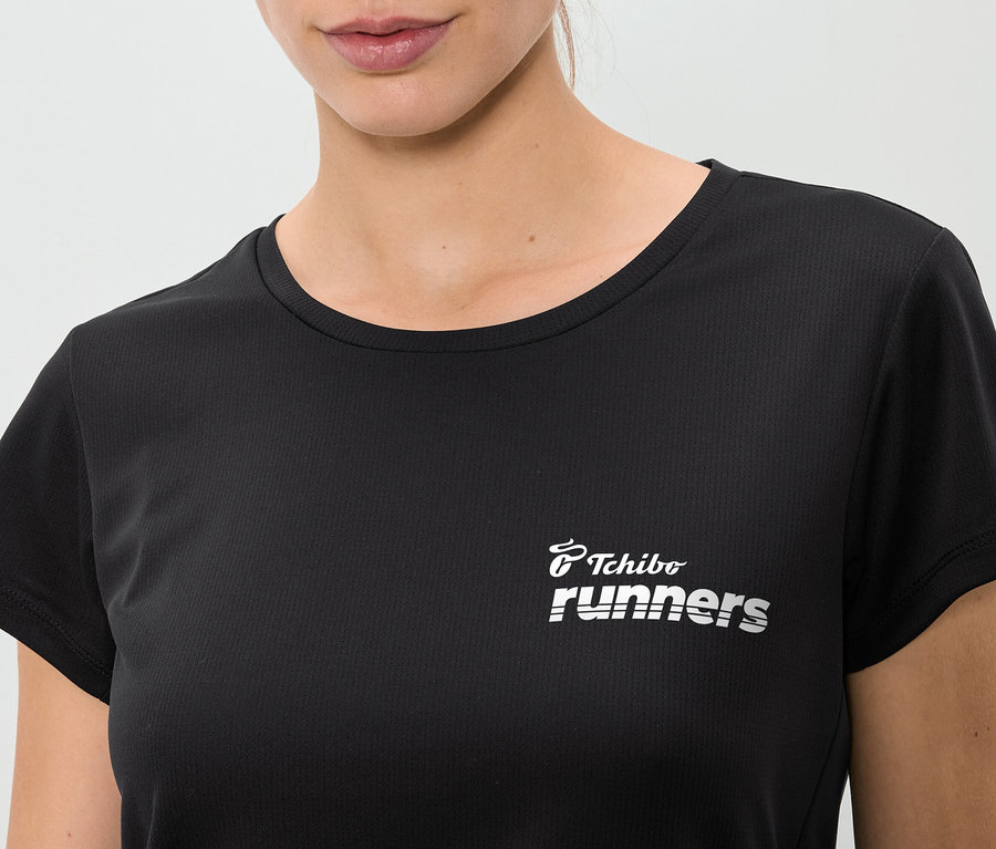Detail ženy v černém tričku s nápisem "Tchibo runners".