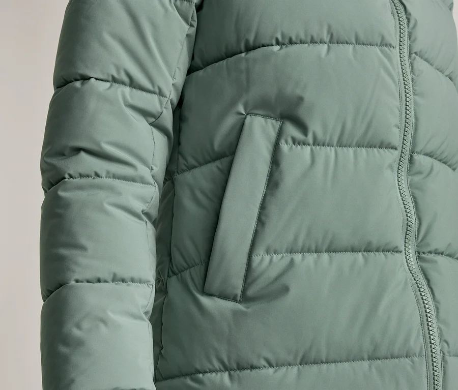 Detailní záběr na mátově zelenou prošívanou bundu se zipem a boční kapsou.