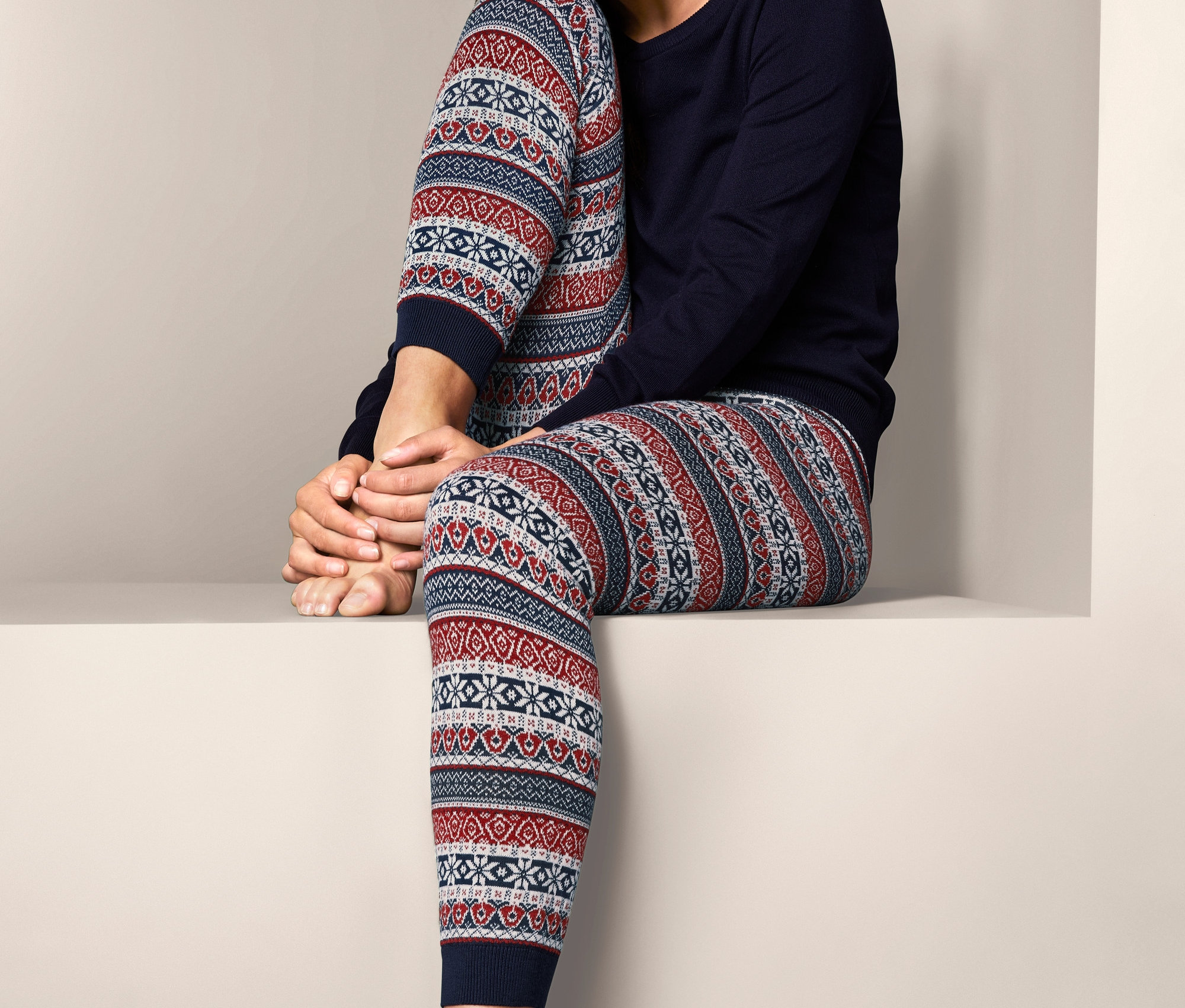 Usmívající se žena sedí a má na sobě pletené legíny s norským vzorem a tmavě modrý top.