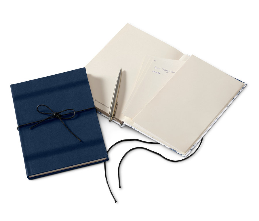 Dva poznámkové bloky, jeden modrý se šňůrkou, druhý otevřený s perem.