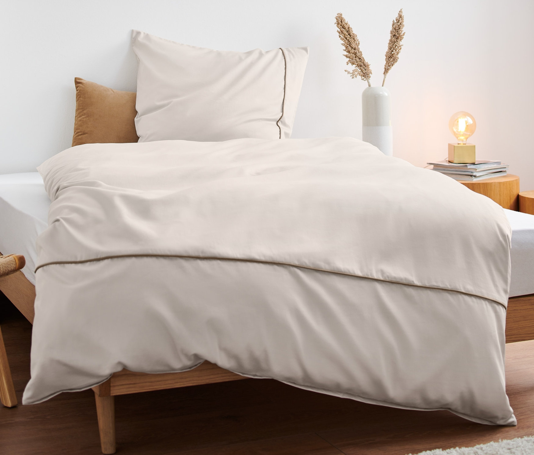 Béžové saténové povlečení prémiové kvality na posteli s dřevěným rámem.