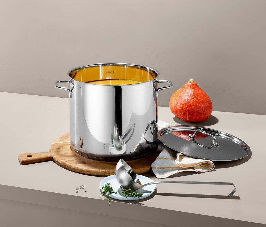 XL hrnec z ušlechtilé oceli stojí na dřevěném prkénku vedle dýně. Poklice a naběračka leží vedle hrnce.